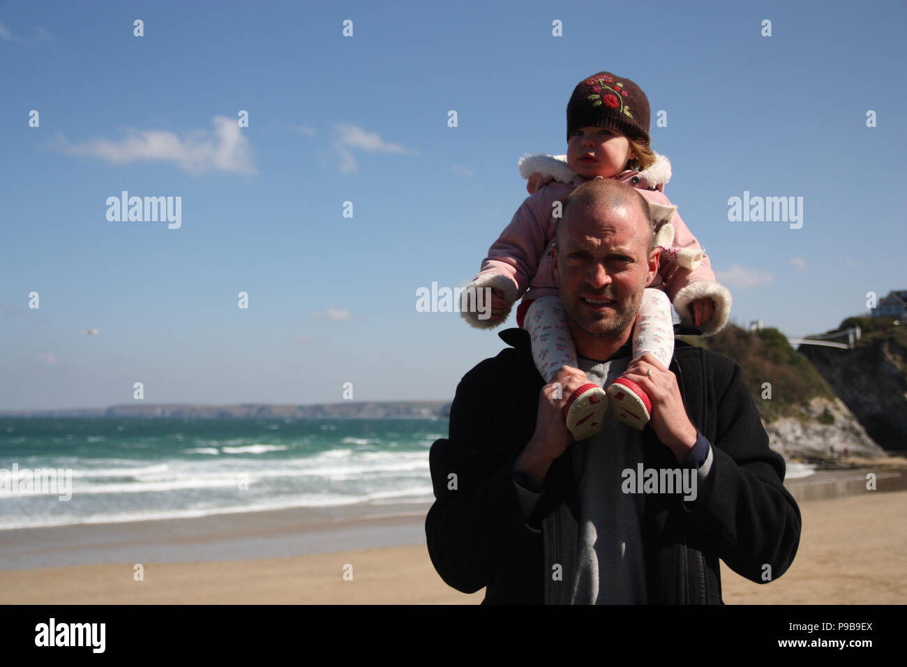 L'uomo con la ragazza sulla sua spalla su di una spiaggia di sabbia in riva al mare a Marazion Cornovaglia Foto Stock