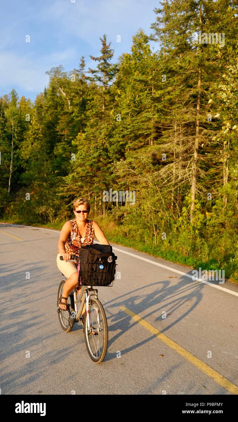 Donna ciclismo su pista ciclabile che circonda l'intera isola di Mackinac, un popolare vechile-free (senza auto) destinazione turistica in Michigan, Stati Uniti d'America. Foto Stock