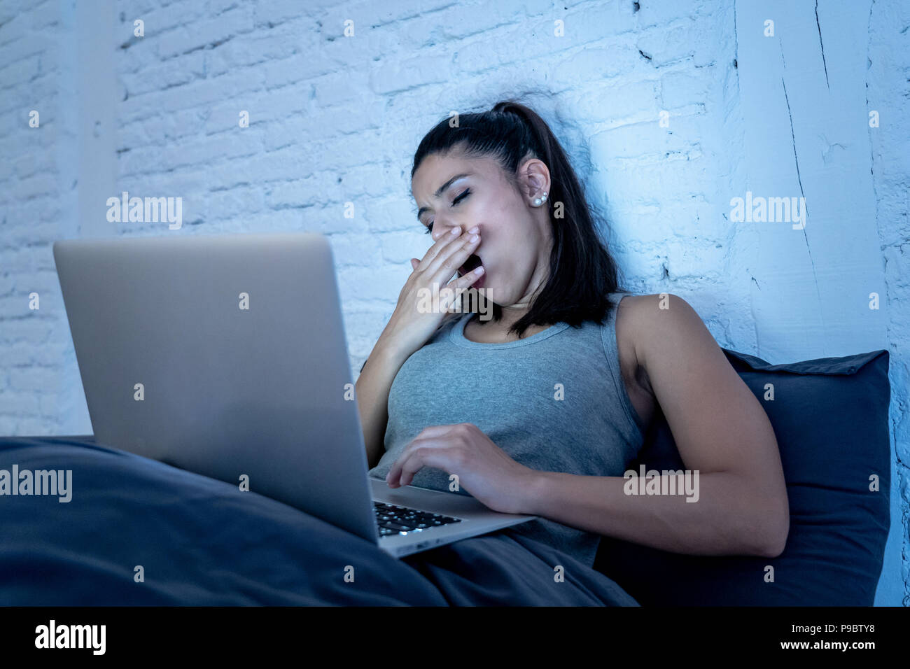 Giovani belle ispanico internet addict donna in pigiama sul letto di casa camera da letto lavorando annoiato e stanco con computer portatile a tarda notte nel buio ro Foto Stock