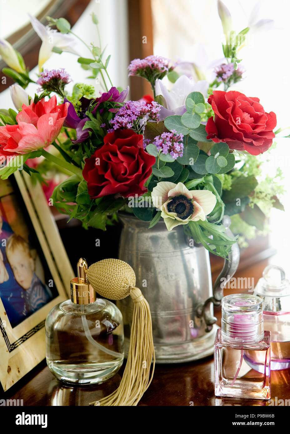 Chiusura del vetro bottiglia di profumo con fiocco e rose rosse con viola verbena bonariensis in argento il boccale Foto Stock