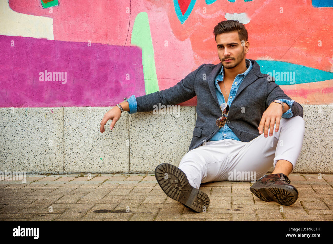 Giovane uomo seduto contro il coloratissimo graffito Foto Stock