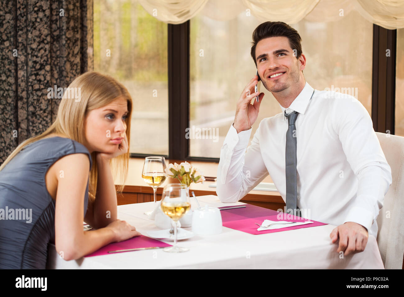 La donna è forata al ristorante, il suo ragazzo parla al telefono Foto Stock