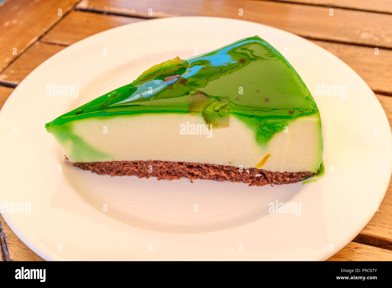 Sezione triangolare di verde smaltato flan soffice torta su un marrone biscotto servito di base su un bianco intorno alla piastra su una tabella woode Foto Stock