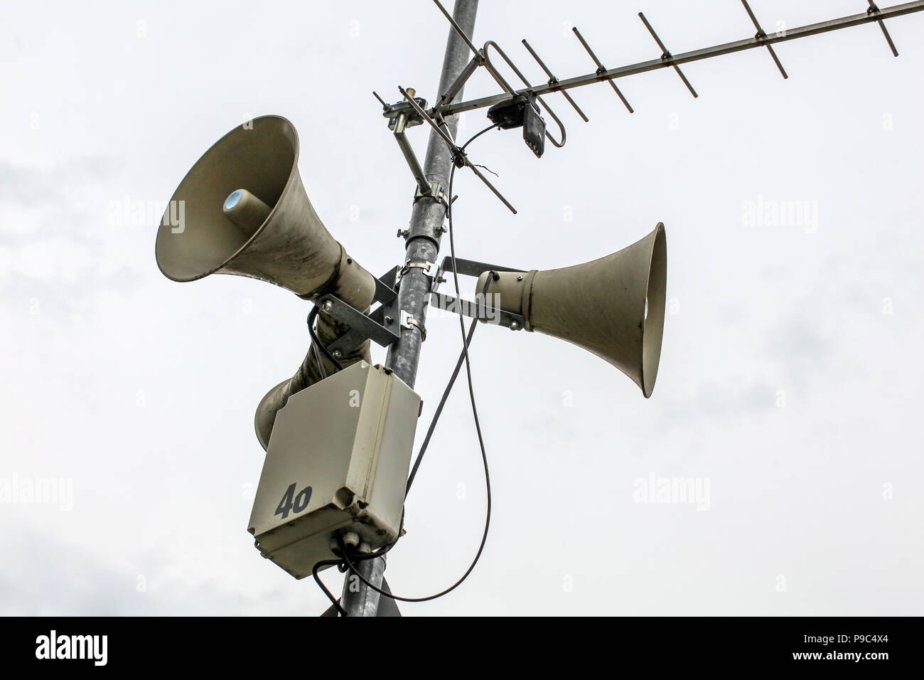 Sistema di comunicazione al pubblico di altoparlanti su un palo, antenna e la casella con il numero 46 parzialmente staccato, cielo nuvoloso in background. Foto Stock