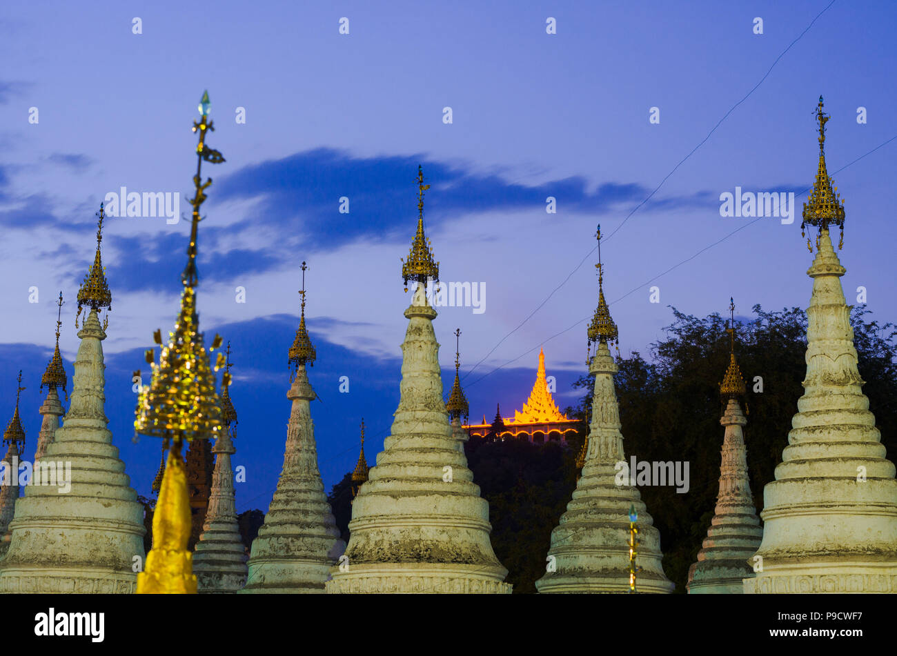 Top guglie di stupa in Sandar Mu Ni Paya, Mandalay con Santuario illuminato in background Foto Stock