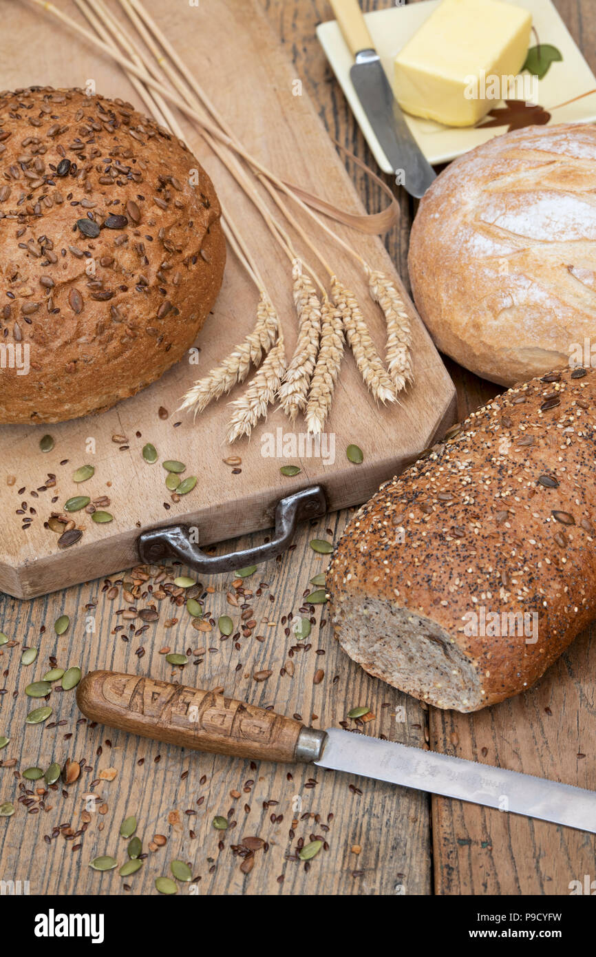 Seminate pane e una focaccia bianca su una scheda di pane di grano e di un coltello per pane. Regno Unito Foto Stock