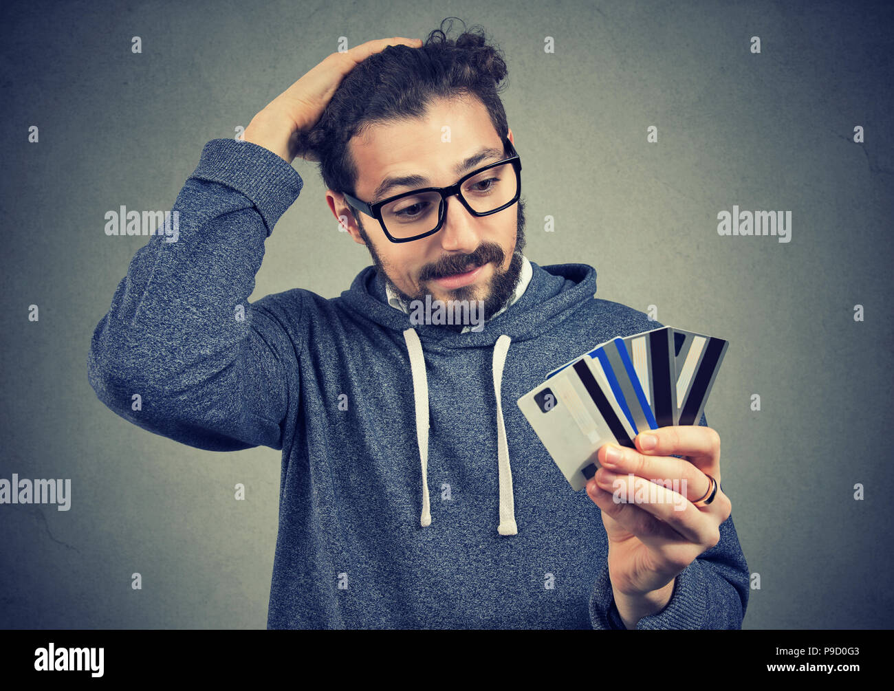 Giovane uomo in bicchieri tenendo le carte di credito e alla ricerca ha sottolineato con debito in aumento Foto Stock