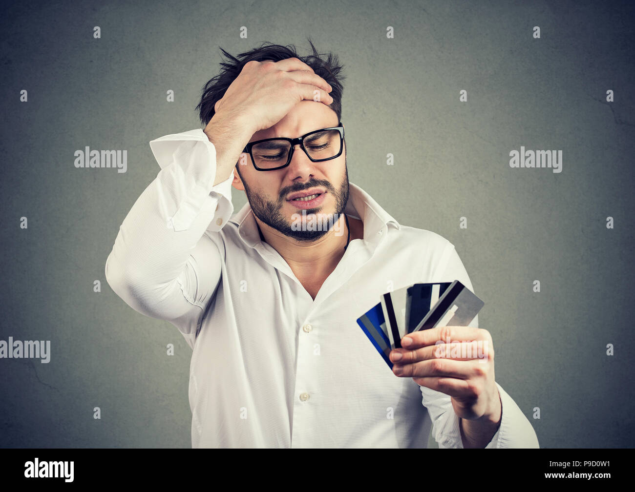 Giovane uomo barbuto in bicchieri e shirt tenendo la mano sulla testa in disperazione avente finanziare debiti per carte di credito Foto Stock