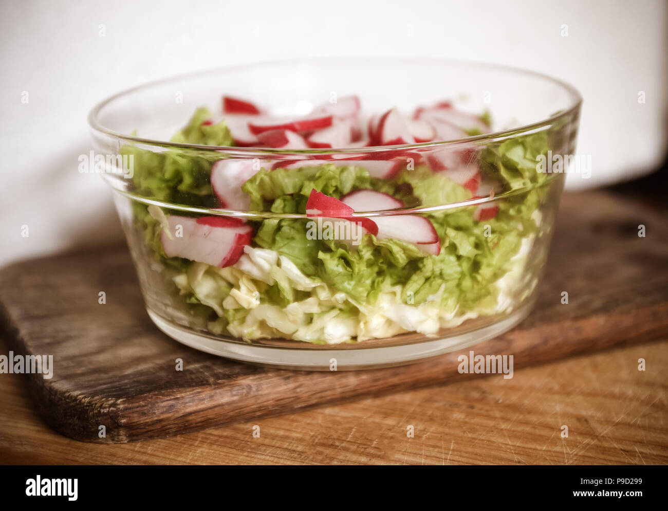 Vegano vegetali insalata di aglio selvatico, Rafano, cipolline, cavolo e lattuga in un grande piatto trasparente su un antico sullo sfondo di legno. Close-up Foto Stock