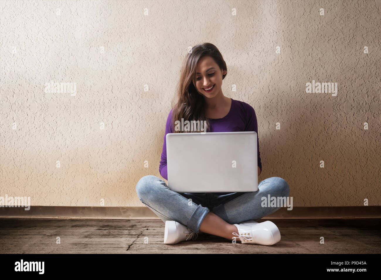 Giovane donna seduta sul pavimento con il computer portatile Foto Stock