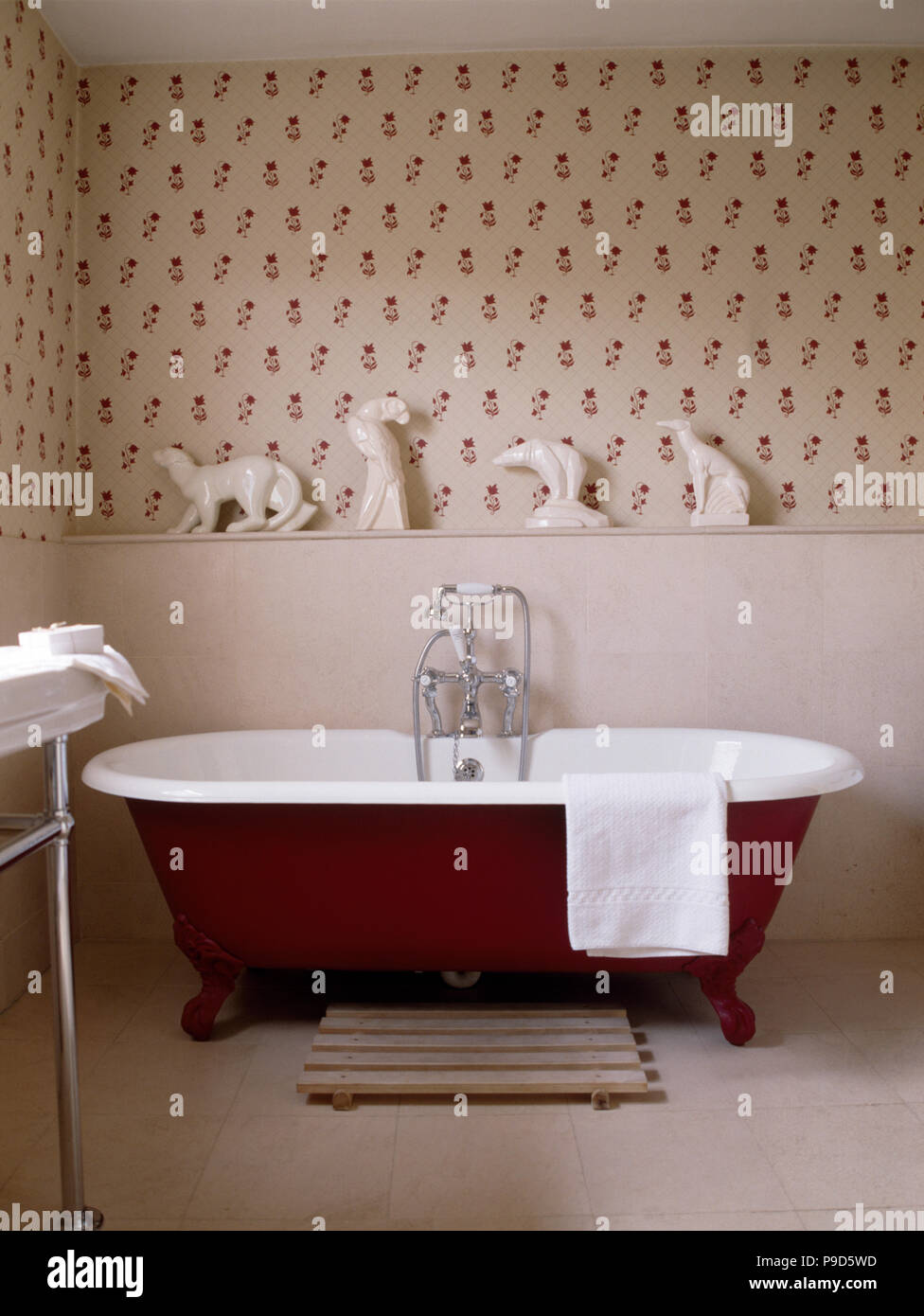 Porcellana Bianca animali sul ripiano sopra un rosso roll top bagno in bagno tradizionale con red sprigged wallpaper Foto Stock