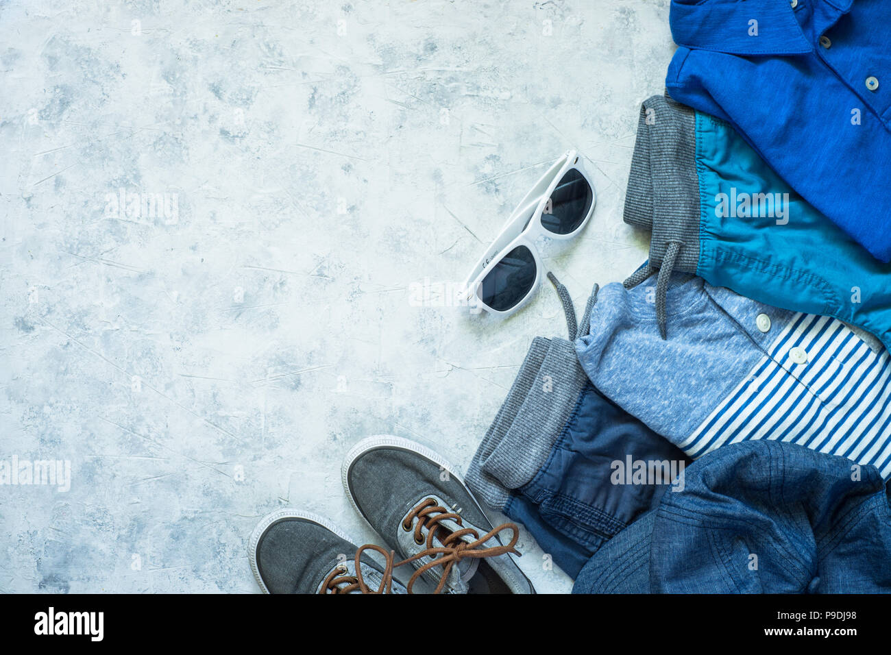 Abbigliamento bambino - jeans, polo, pantaloncini corti e scarpe da ginnastica vista dall'alto su sfondo di pietra. Moda & Bellezza dello sfondo. Look moderno. Piatto copia laici spazio. Foto Stock