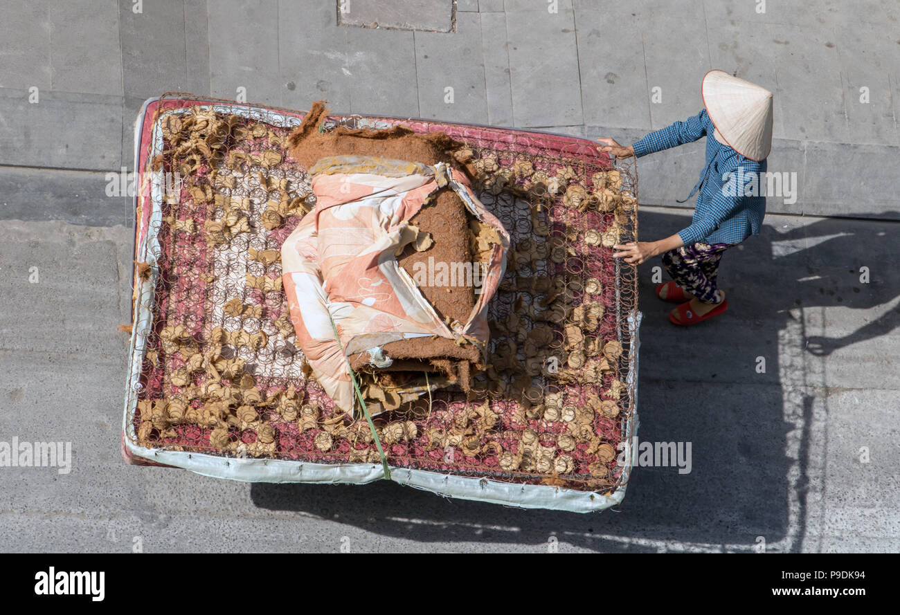 Donna vietnamita spingendo un carrello con un grande vecchio materasso. La vita sulla strada a Saigon city. Foto Stock