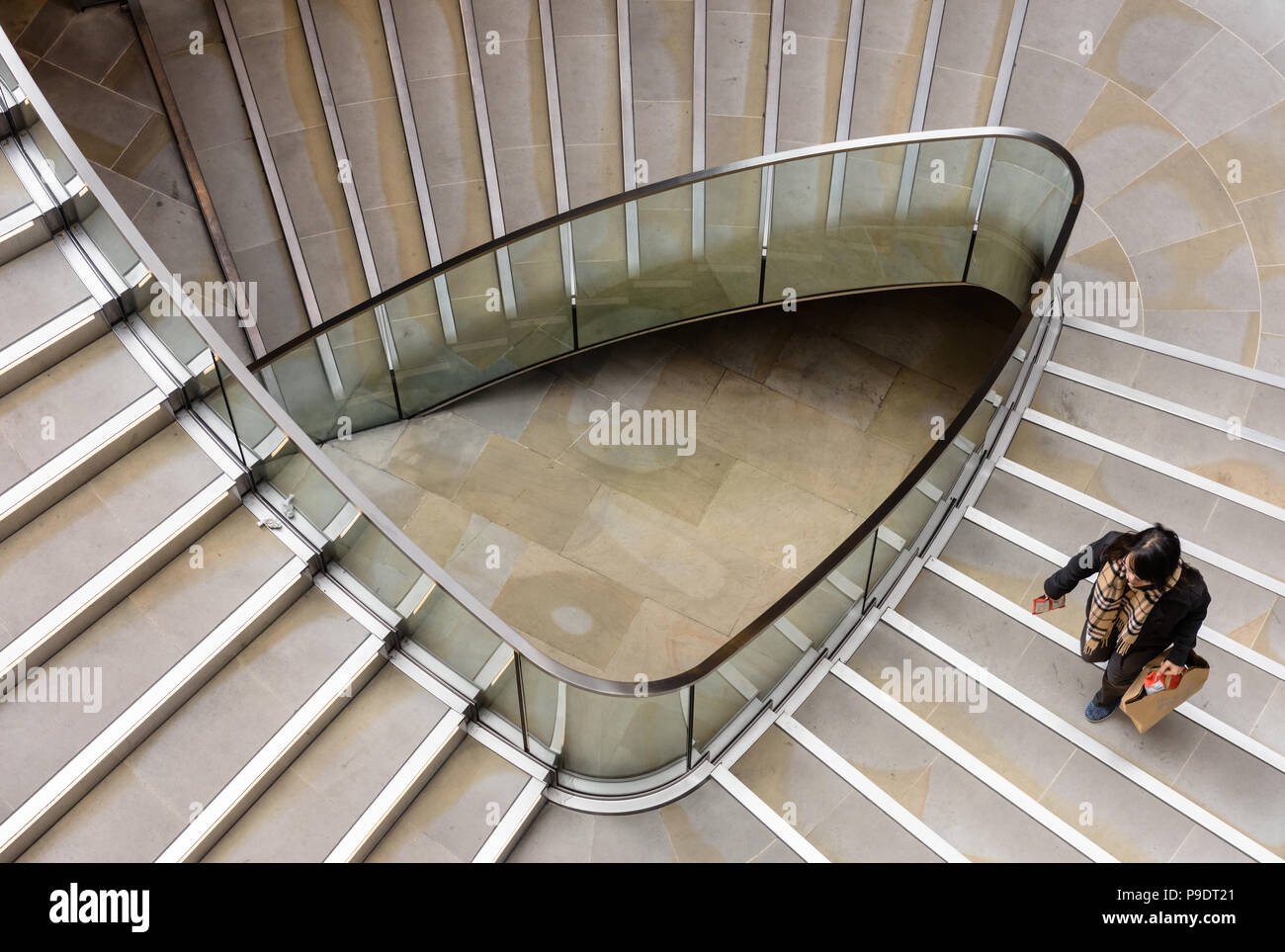 Donna che trasportano shopping bag fino a triangolare di scala a chiocciola in Londra Foto Stock