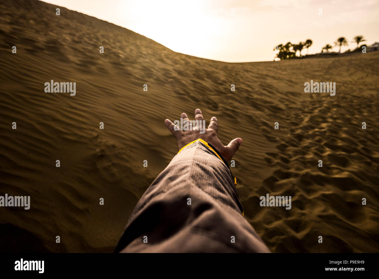 Mano e braccio maschio pronto a toccare e raggiungere l'orizzonte nel deserto arido senza acqua. oeasis in backgorund. dune e sabbia e il footprint di PEO Foto Stock