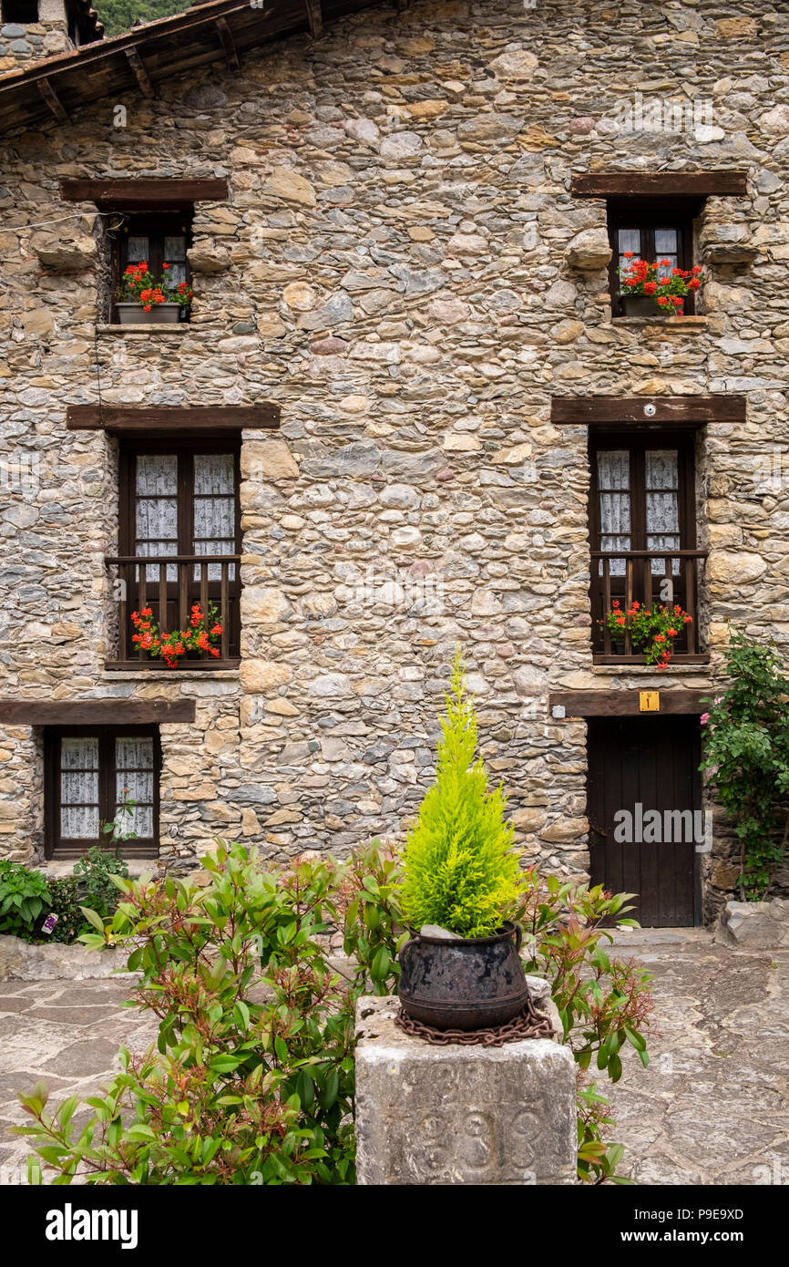 Pietra di granito facciata di casa con gerani crescendo in scatole di finestra in Pyreneean villaggio di generare, Catalogna, Spagna Foto Stock