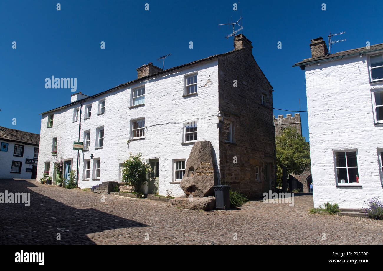 Strada principale lastricata in pietra di ammaccatura village nel Yorkshire Dales National Park, con Adam Sedgwick monumento. Foto Stock