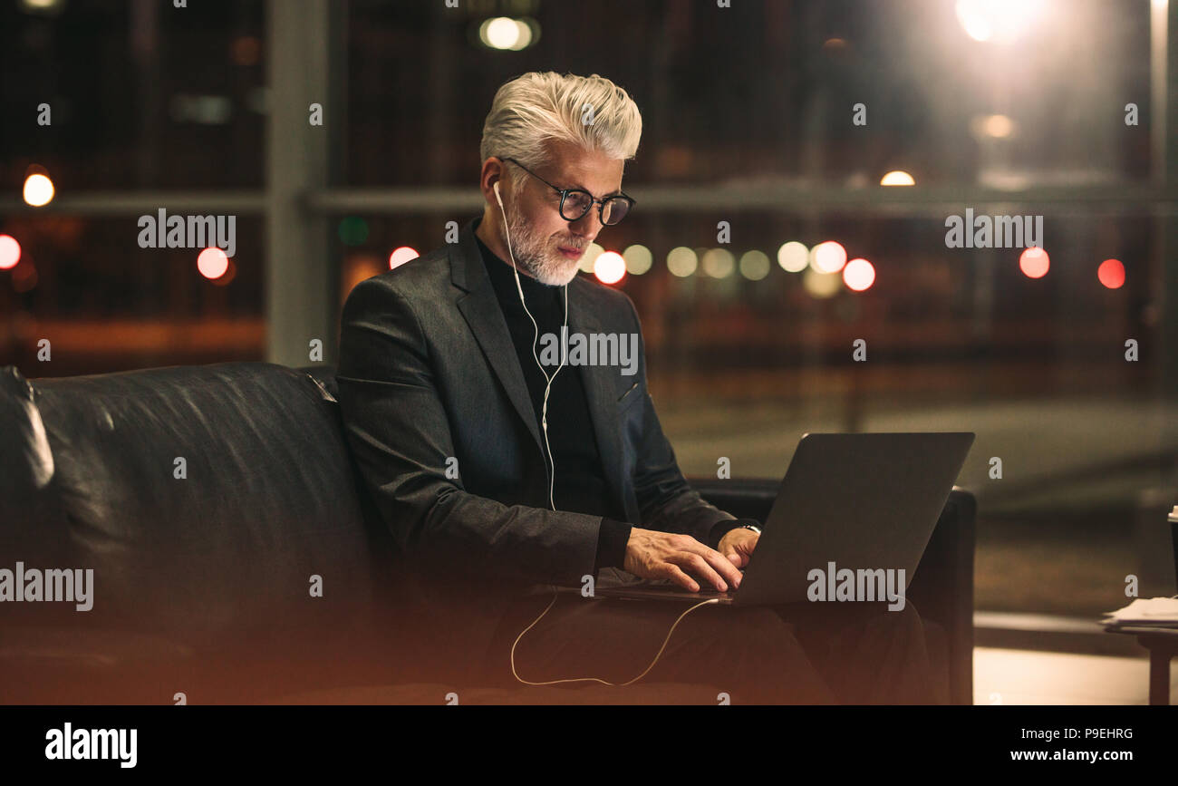 Imprenditore maturo lavorando su laptop a tarda notte in ufficio. Uomo caucasico in business vestiti emis sione di computer portatile in ufficio lobby. Foto Stock