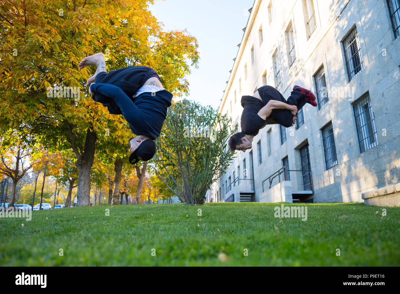 Due giovani uomini facendo un lato flip o capriola mentre essi praticano parkour sulla strada. Foto Stock