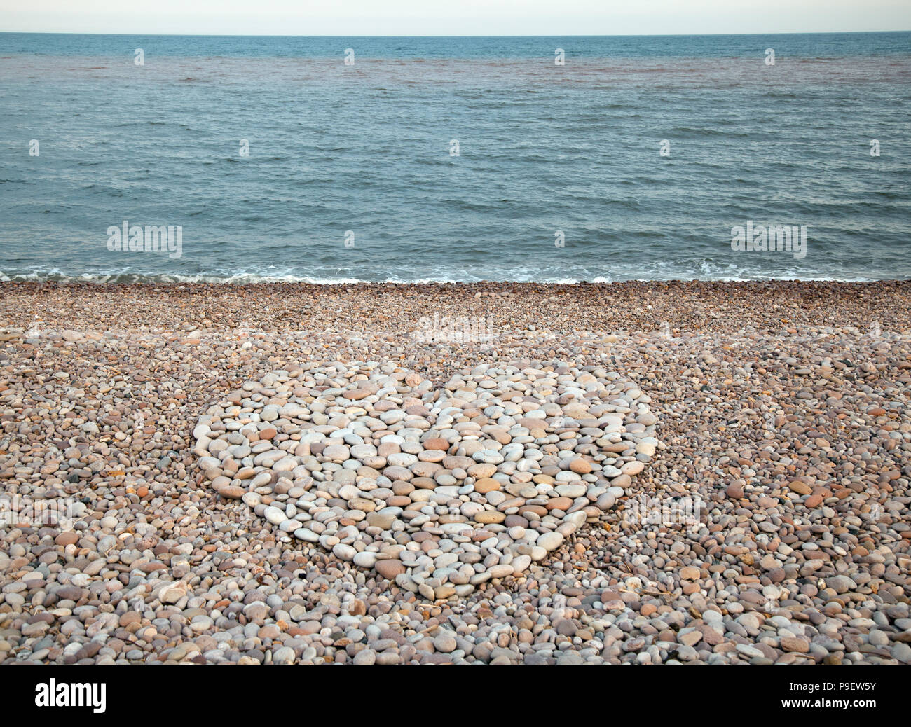 Un cuore di posizionamento sagomati di ciottoli su Budleigh Salterton beach Foto Stock