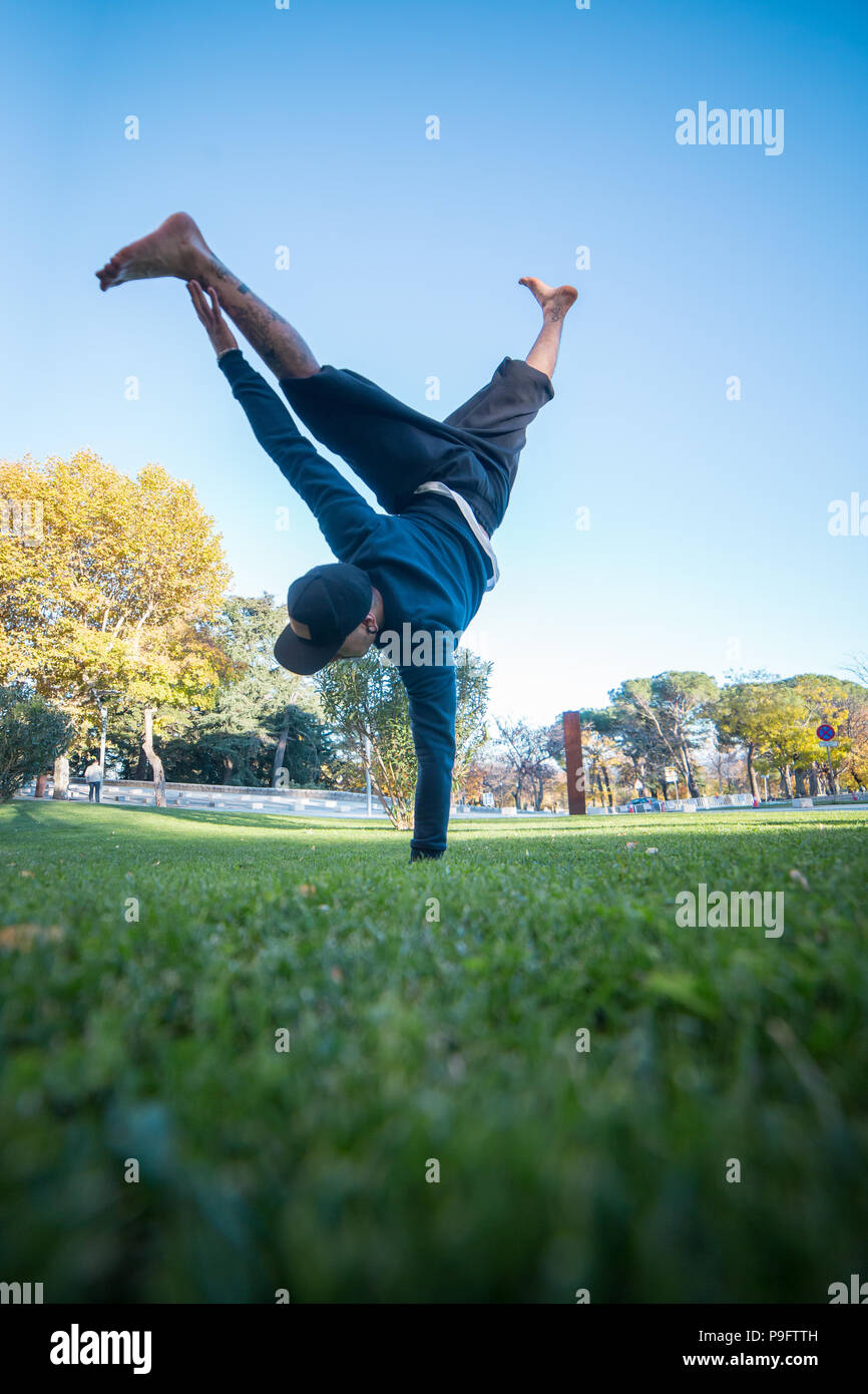 Giovane uomo facendo handstand sull'erba in strada mentre fa parkour. Foto Stock