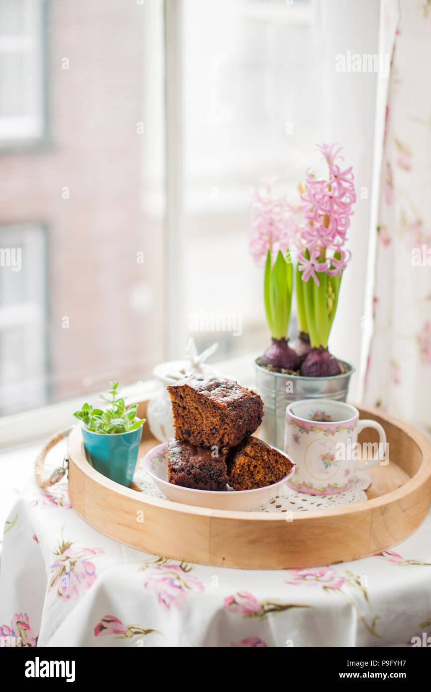 Tortina di cioccolato con zucchero e caffè. La colazione su un vassoio di legno e fiori. La vista dalla finestra per la città. Foto Stock