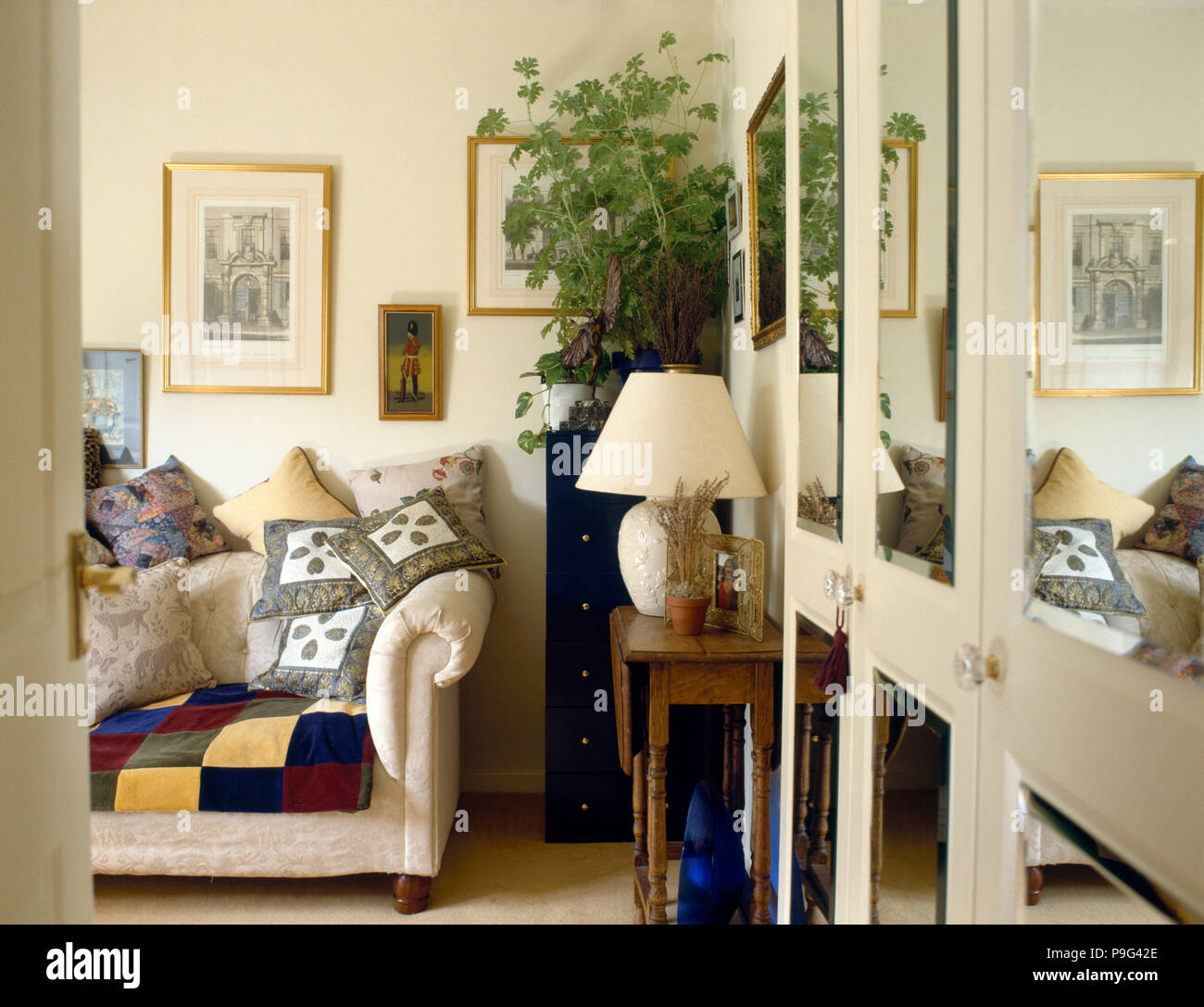 Cuscini impilati sul divano color crema in novanta soggiorno con pannelli a specchio sulle antine Foto Stock