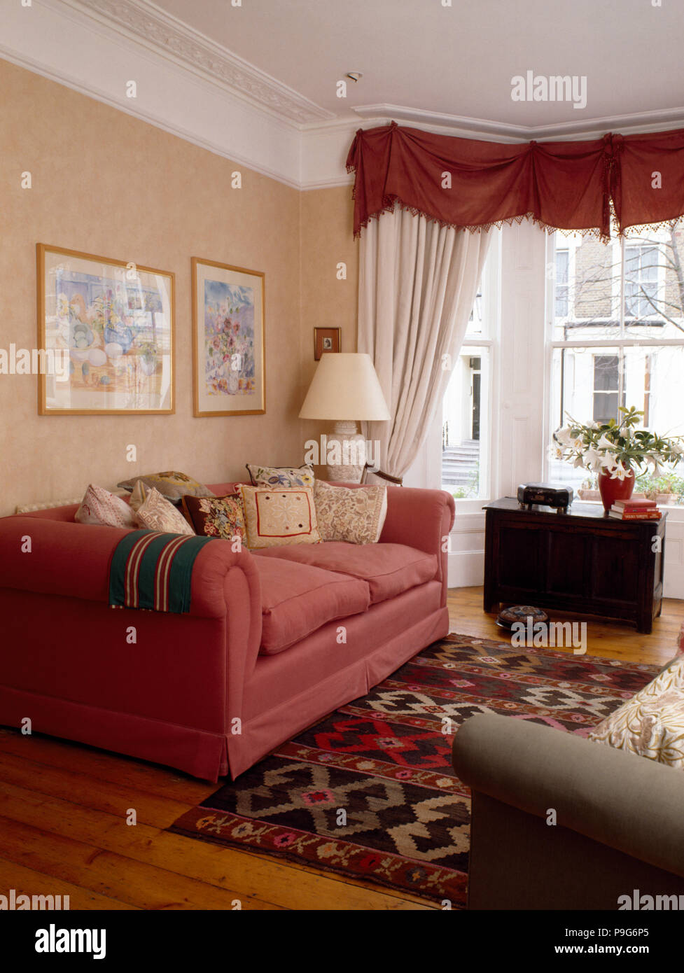Divano rosa degli anni novanta in soggiorno con una rosa mantovane e tendaggi bianchi sulla finestra Foto Stock