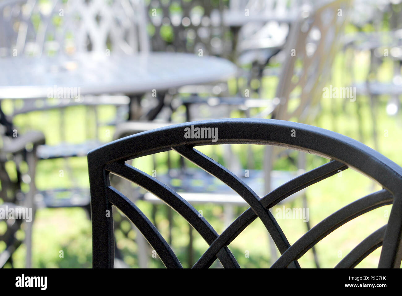 Close up di un ferro battuto sedia, con altri simili e i tavoli e le sedie in fuori fuoco sfondo su una bella giornata di sole Foto Stock
