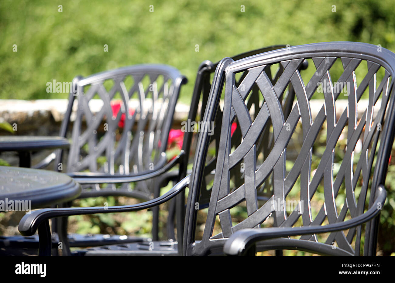 Close up di un ferro battuto sedia, con altri simili e i tavoli e le sedie in fuori fuoco sfondo su una bella giornata di sole Foto Stock