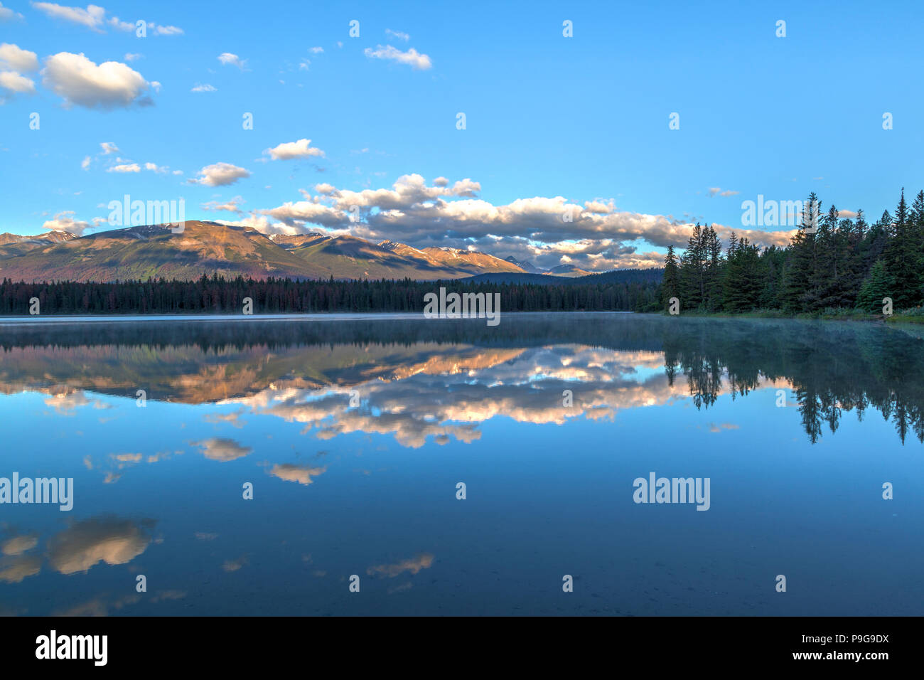 Sole al mattino e nuvole basse coprono le montagne rocciose a Annette lago nel Parco Nazionale di Jasper con riflessi del Majestic Mountain e Aquila Mountain Foto Stock