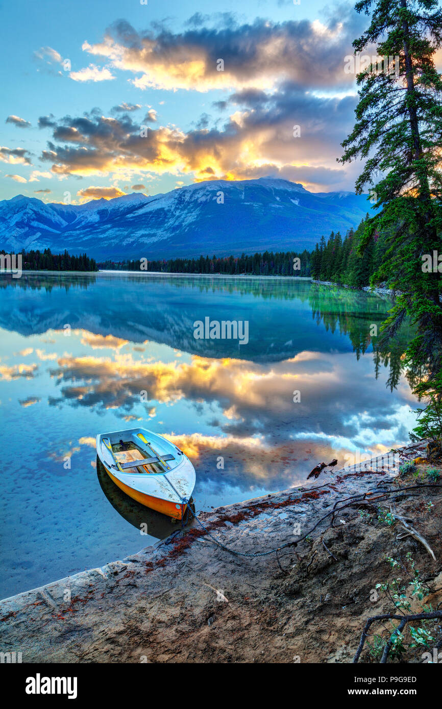 Sole di mattina si rompe sulle Montagne Rocciose ad Edith lago nel Parco Nazionale di Jasper, con una barca in primo piano. Foto Stock