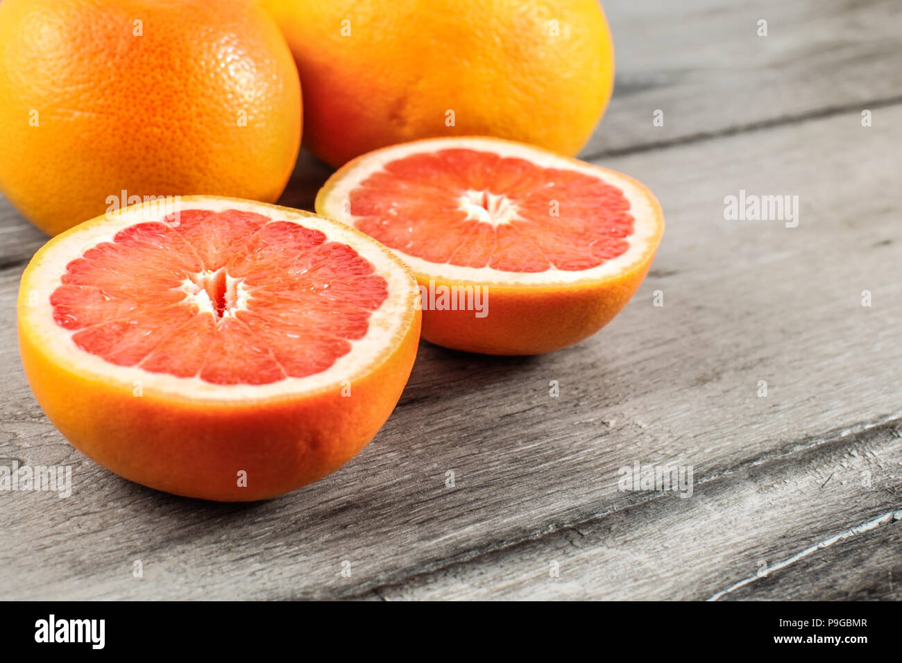 Rosa rosso pompelmo tagliato a metà con due interi in sfondo grigio sulla tavola di legno. Foto Stock