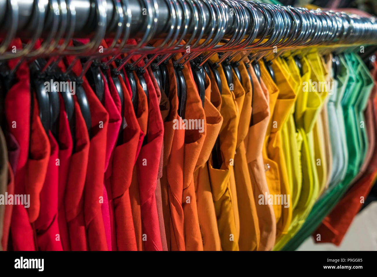 Maschio di uomini camicie ordinati in ordine di colore su appendiabiti su un negozio di parsimonia o guardaroba rail Foto Stock