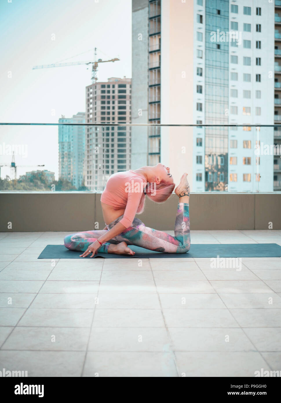 Giovane donna slim con rosa capelli tinti facendo yoga pratica sulla terrazza della città moderna. Ragazza per tenersi in forma e corpo sano relax sulla terrazza sul tetto durante la pratica, rappresentano Foto Stock