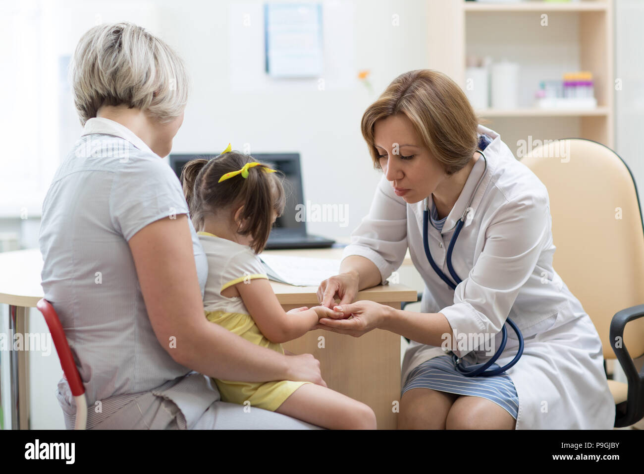 Medico pediatra azienda kid la mano nelle sue mani. Bambino ragazza seduta a madre sulle sue ginocchia Foto Stock