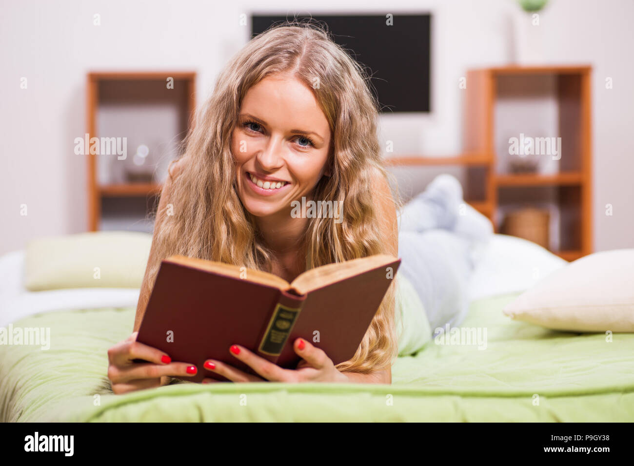 Giovane donna è sdraiato sul letto e la lettura del libro. Foto Stock