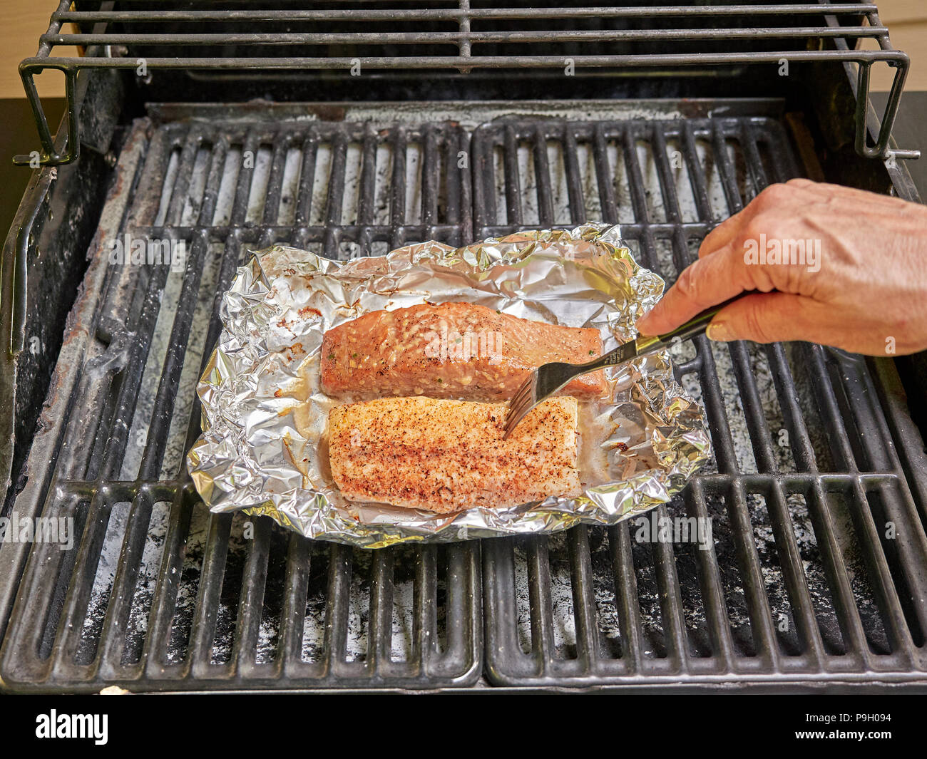 La cottura di salmone e bianco i filetti di pesce su un grill all'aperto utilizzando la stagionatura. Foto Stock