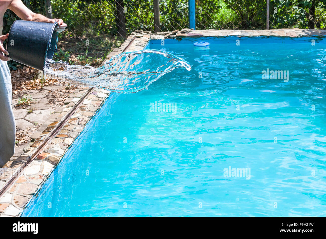 L uomo si riversa di disinfettante dal bucket in piscina esterna sul cortile della casa di paese Foto Stock