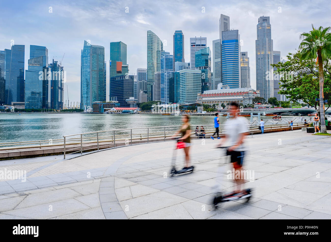 Moderno skyline di Singapore con grattacieli, persone a cavallo kick scooters in città embankment Foto Stock
