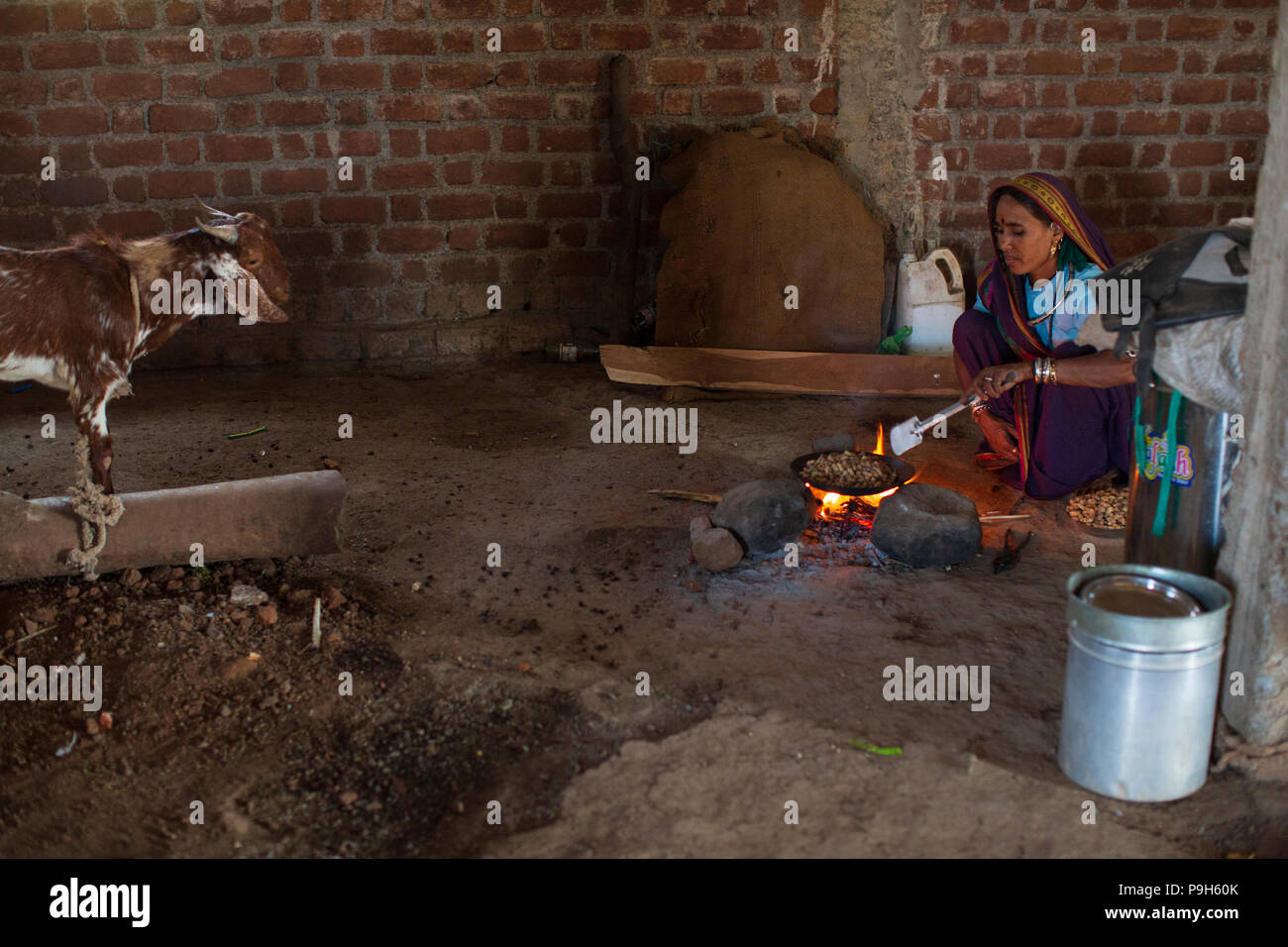 Una donna la tostatura arachidi su un fuoco aperto in casa loro a Sendhwa rurale, India. Foto Stock