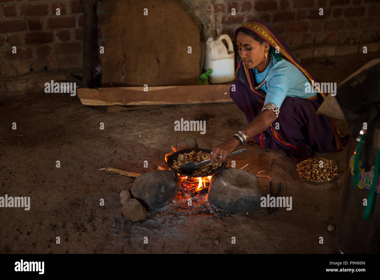 Una donna la tostatura arachidi su un fuoco aperto in casa loro a Sendhwa rurale, India. Foto Stock