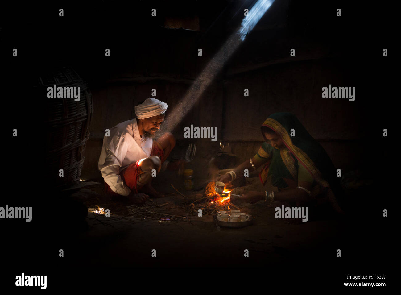 Un marito e una moglie rendono Indian chai su un fuoco aperto nella loro casa, Indore, India. Foto Stock