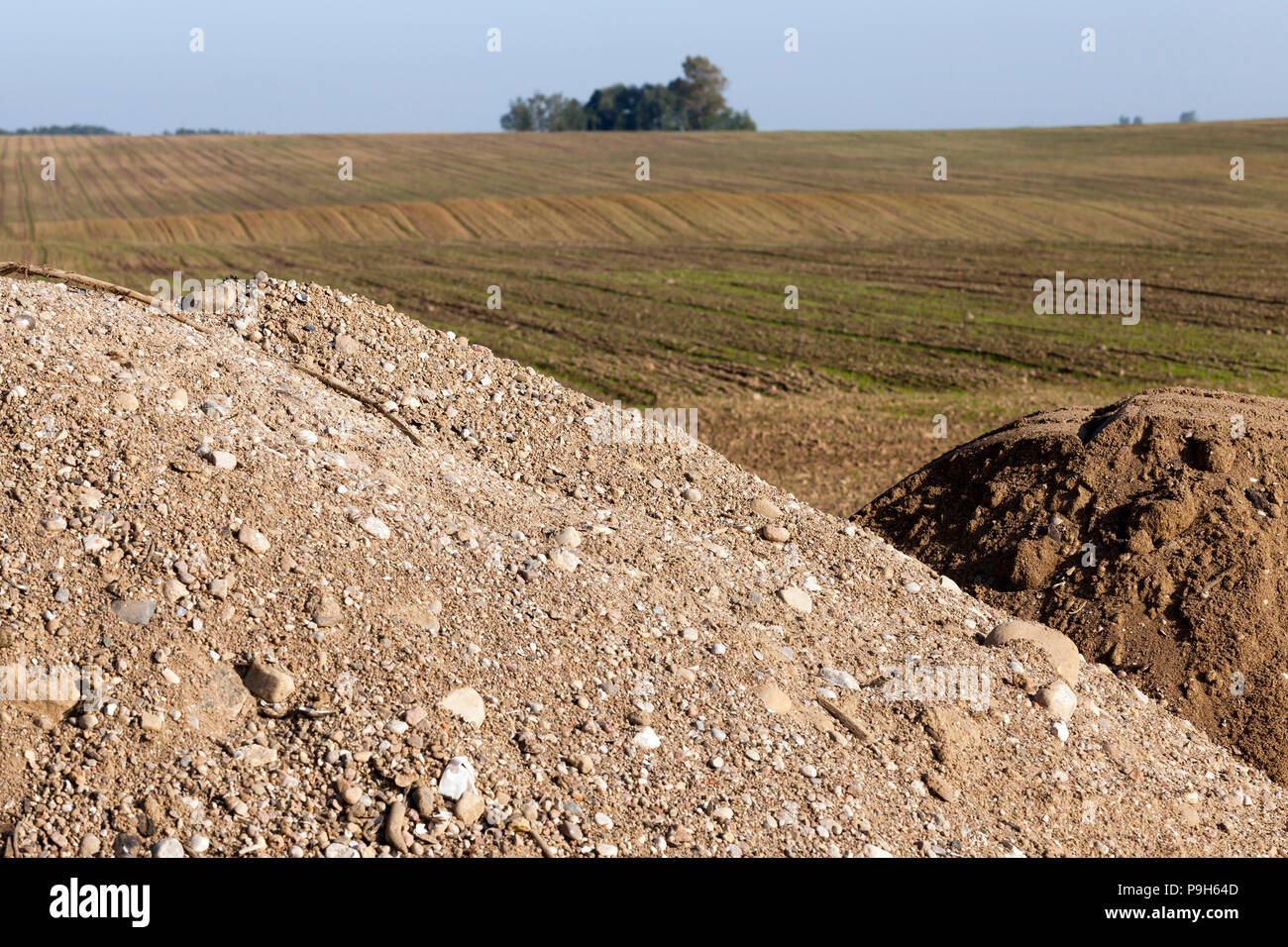 Un gran mucchio di sabbia, ghiaia e altri materiali da costruzione nel campo vicino alla strada riparato Foto Stock