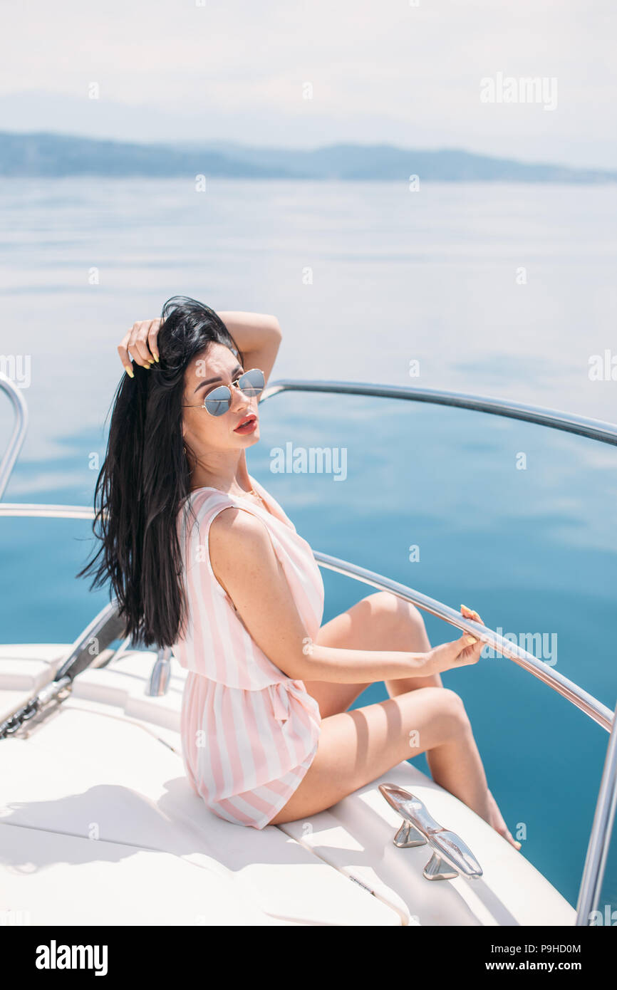 Giovane, attraente e ricca imprenditrice caucasica si impegna con uno yacht, avente fotossesion su una barca di lusso in mare al giorno d'estate e di sole Foto Stock