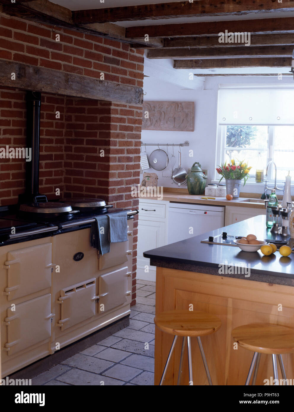 La crema Aga in una cucina di paese con un esposto un muro di mattoni e legno rustiche travi a soffitto Foto Stock