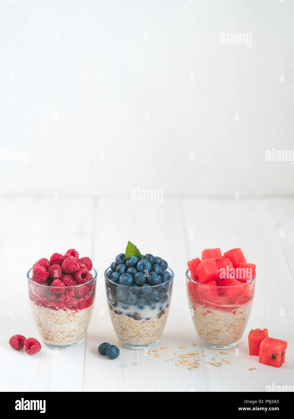 Sana colazione:durante la notte di avena con frutta fresca e bacche di vetro.Durante la notte i fiocchi d'avena porridge con cocomero,lampone, mirtillo,decorate menta. Per una notte di avena sul tavolo bianco,spazio copia.Vertical Foto Stock