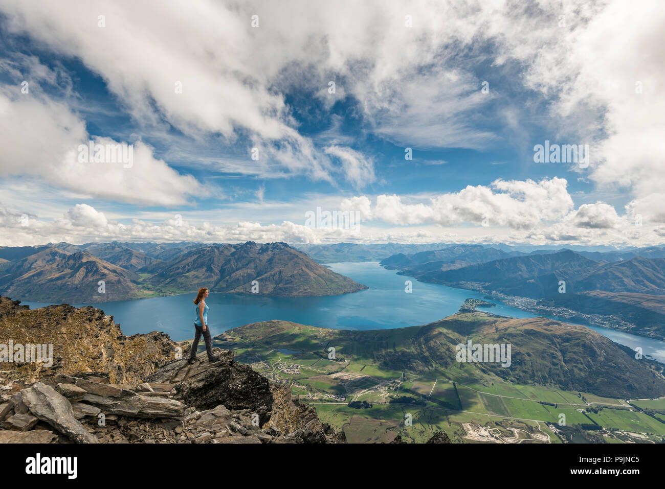 Escursionista femmina sorge su rocce del Remarkables, affacciato sul lago Wakatipu e sulle montagne e Queenstown, Queenstown, Otago Foto Stock