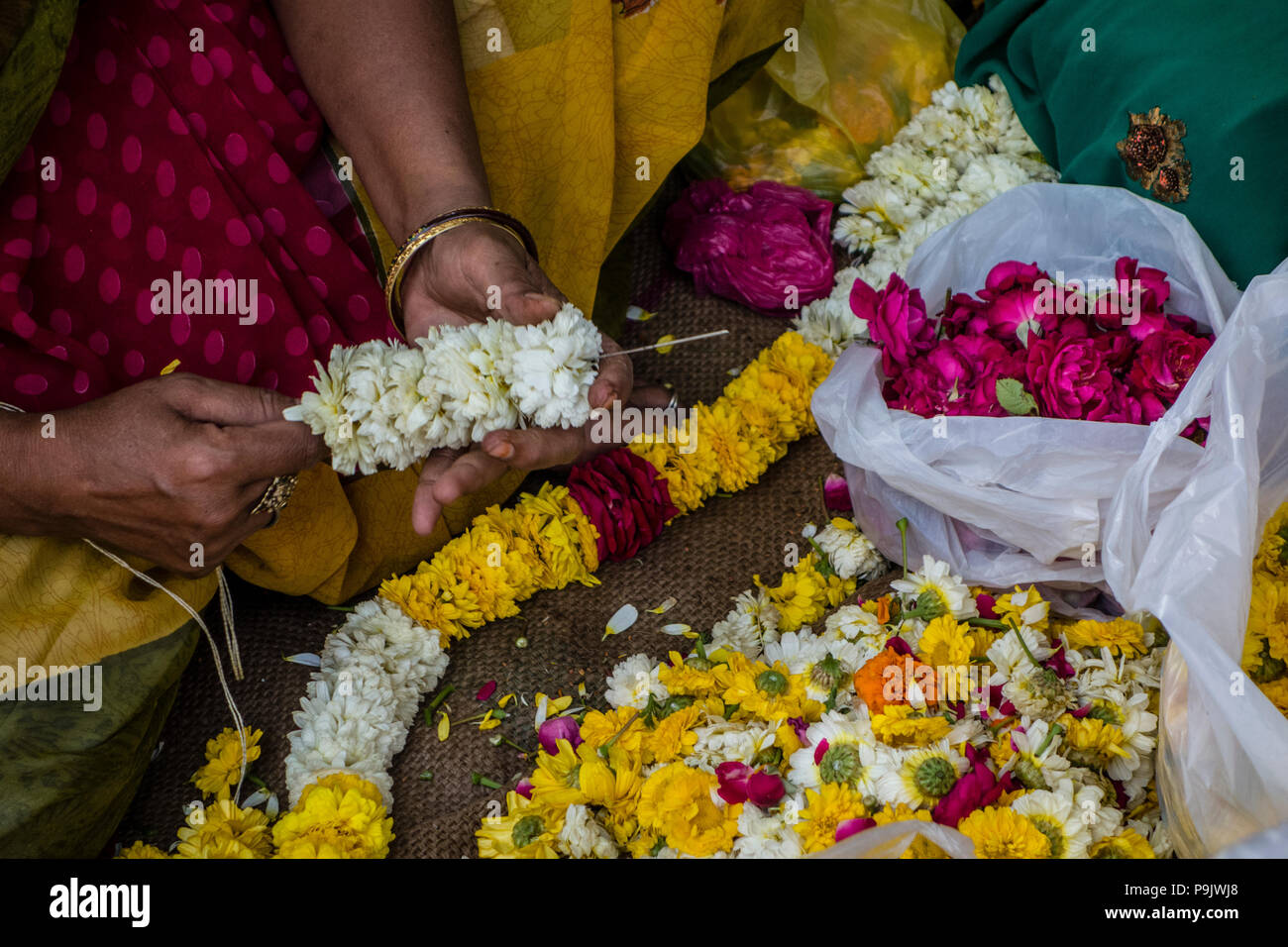 Donna indiana rendendo tradizionali di ghirlande di fiori in un mercato in stallo la Vecchia Delhi, Delhi, India Foto Stock