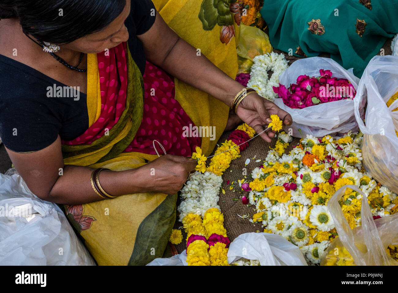 Donna indiana rendendo tradizionali di ghirlande di fiori in un mercato in stallo la Vecchia Delhi, Delhi, India Foto Stock